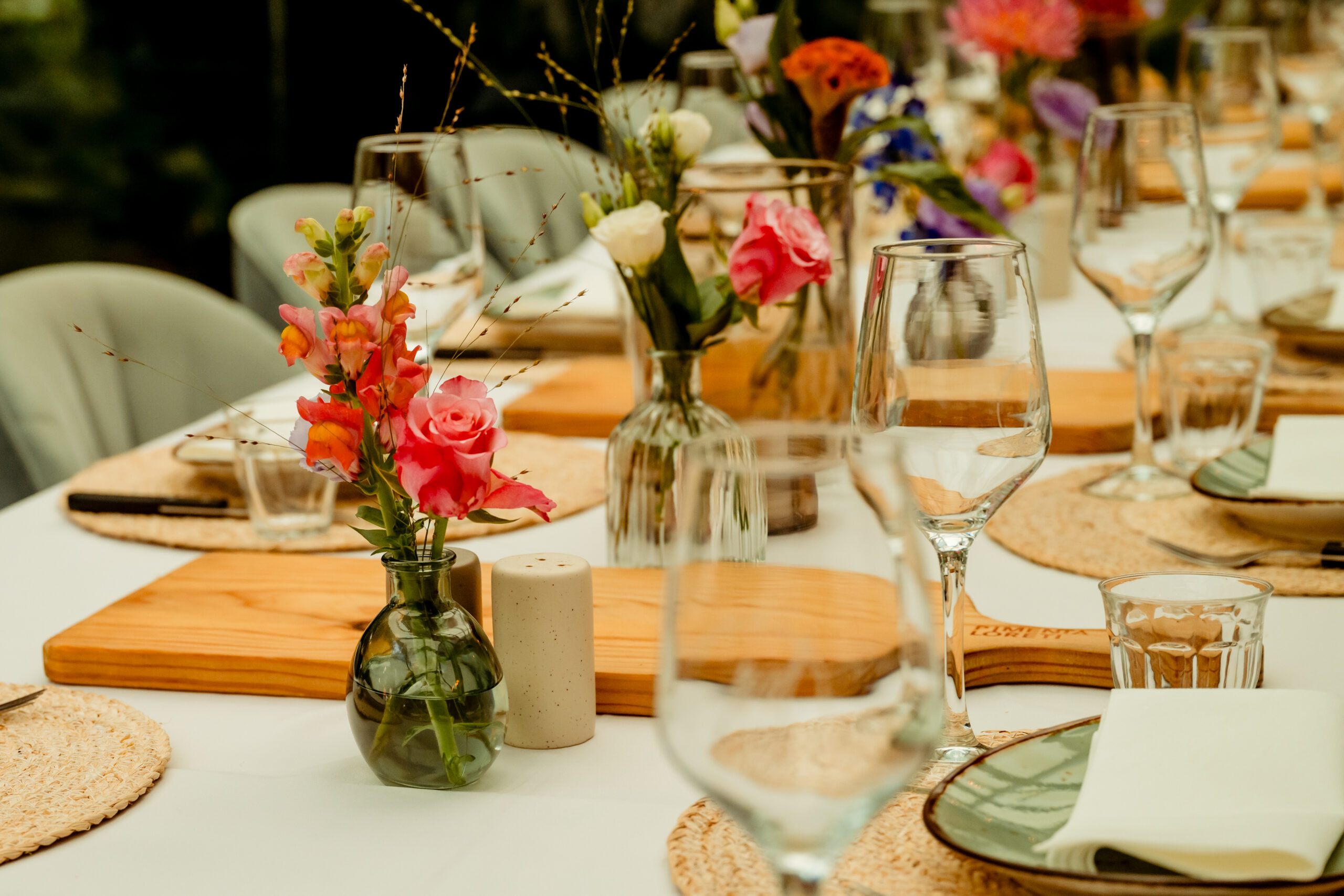 Lange gedekte tafel met bloemen in kleine vaasjes, houten planken en glazen, klaar voor het diner