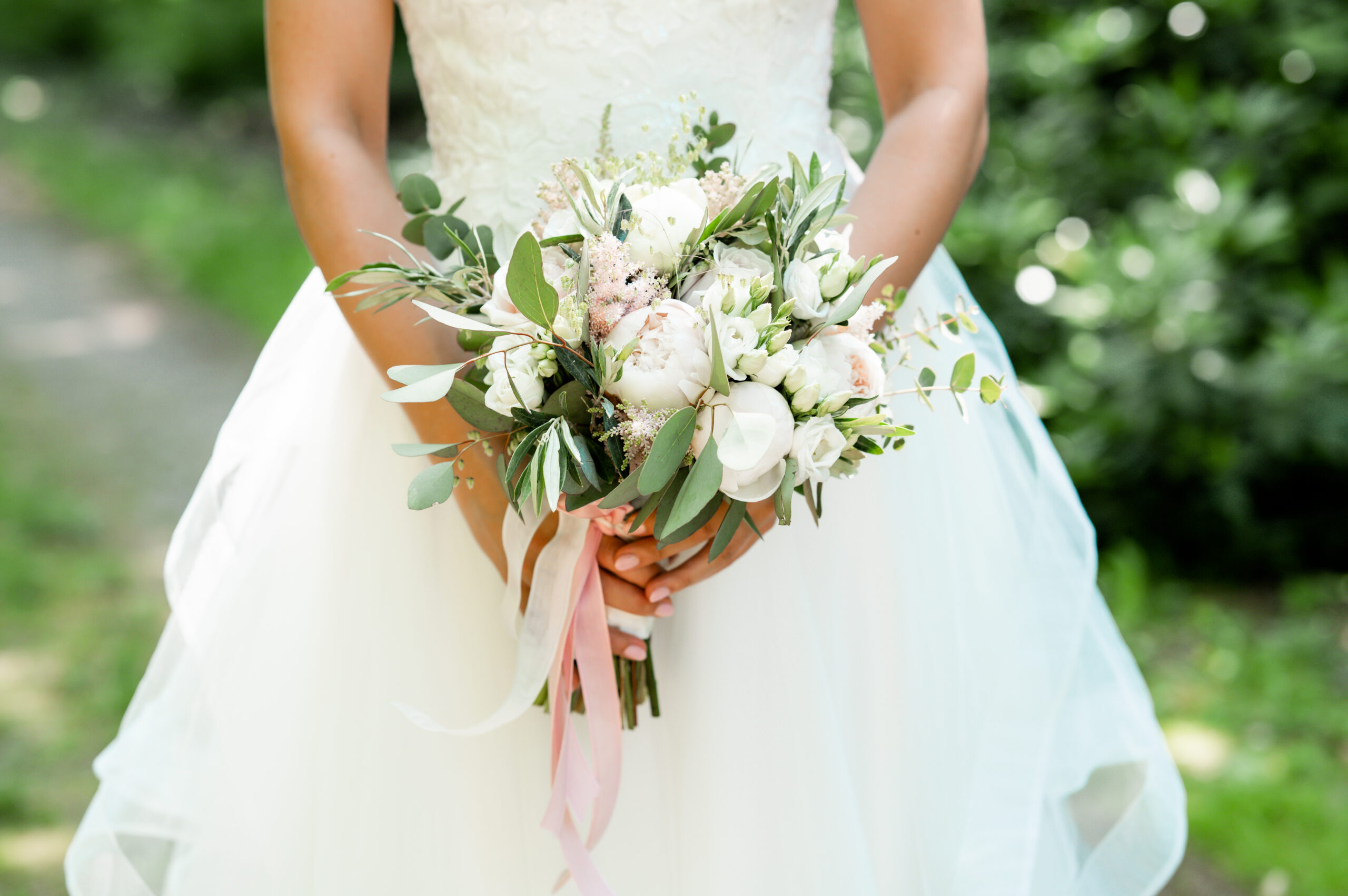 Bruid houdt een boeket met witte en roze bloemen en een roze lint vast