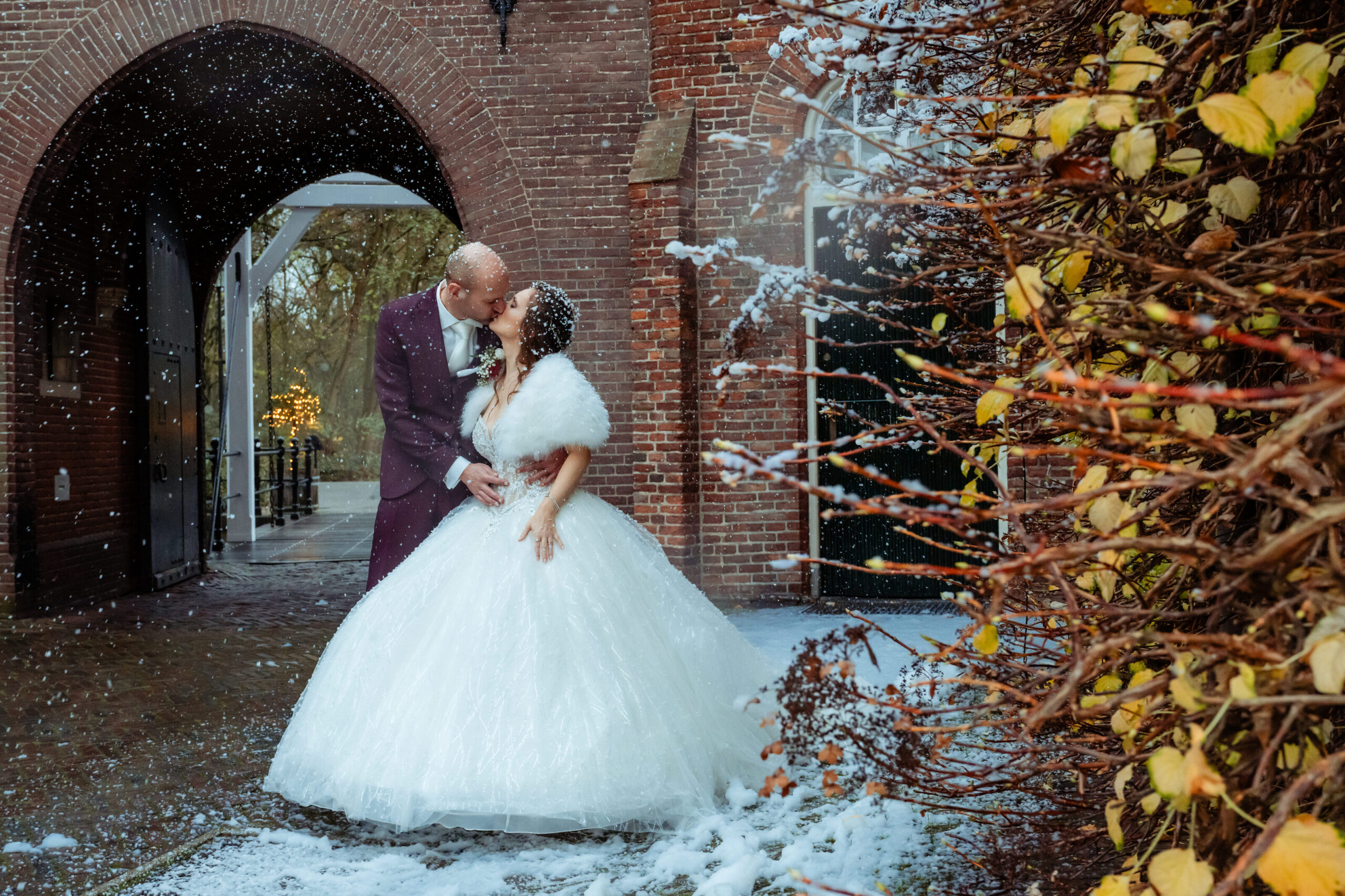 Bruidspaar kust in de sneeuw onder de poort van Kasteel Maurick