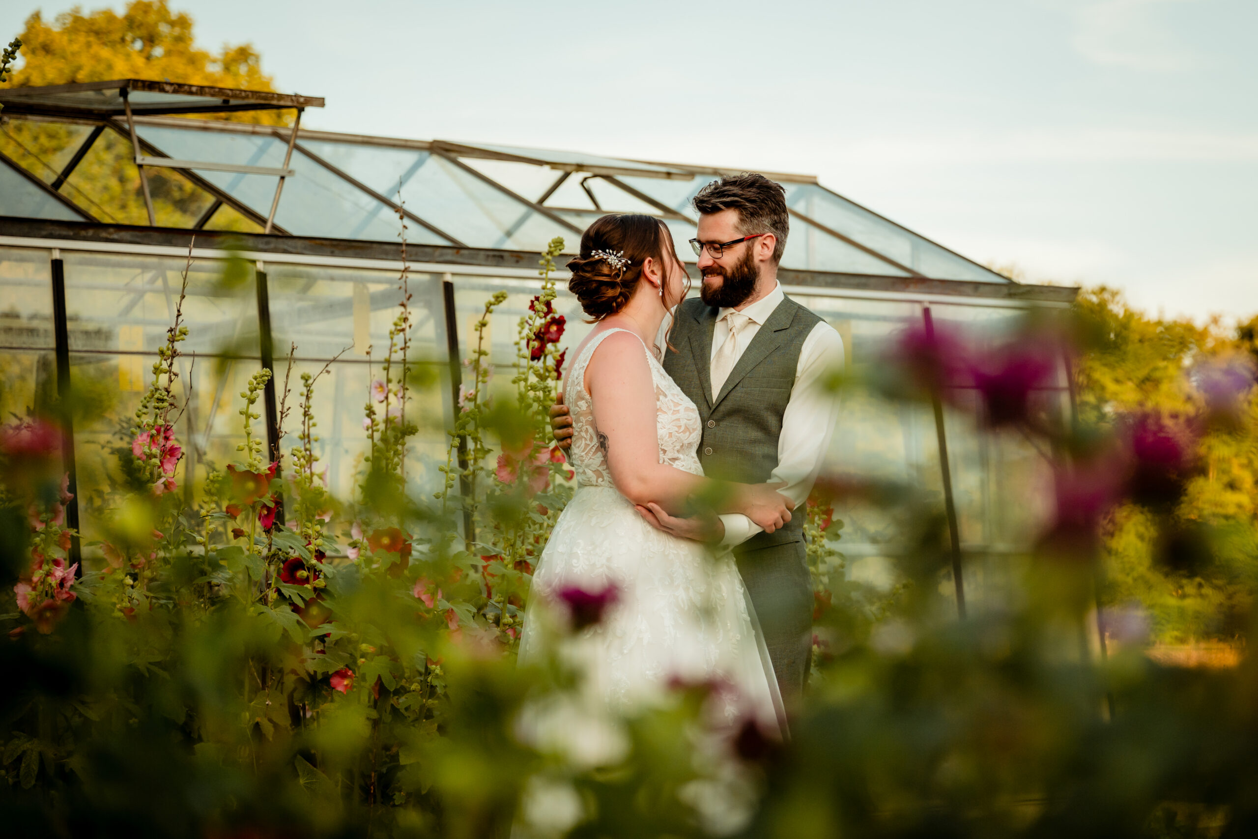 Bruidspaar tijdens golden hour bij oude kas met bloemen