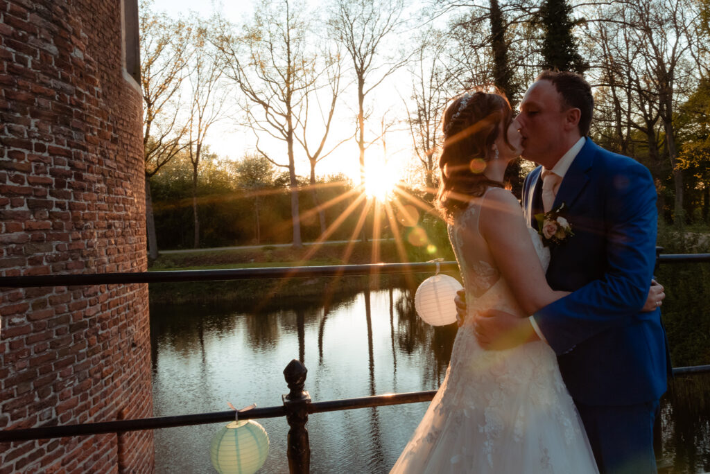 Bruidspaar kust elkaar bij zonsondergang aan de slotgracht van Kasteel Dussen