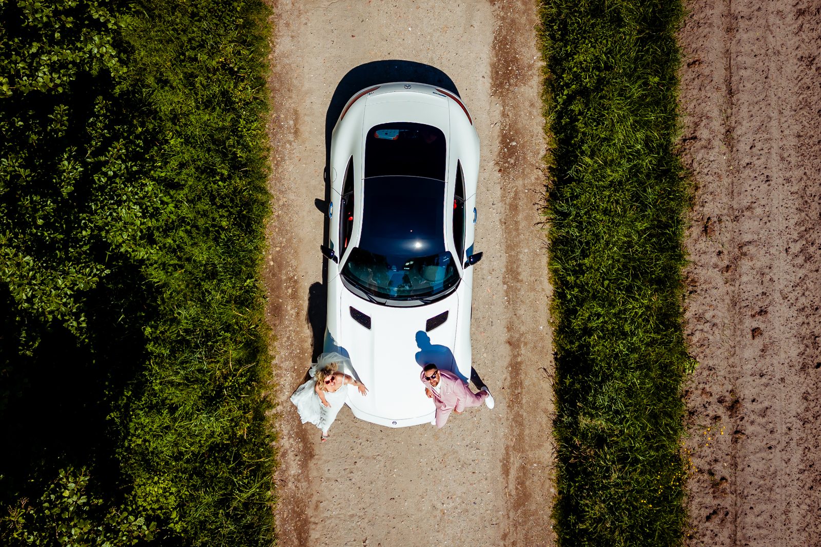 Trouwauto op een zandpad tussen de velden, dronefoto recht van boven